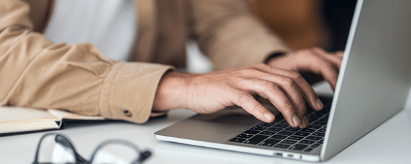 Hands type on a laptop sitting on a white desk.