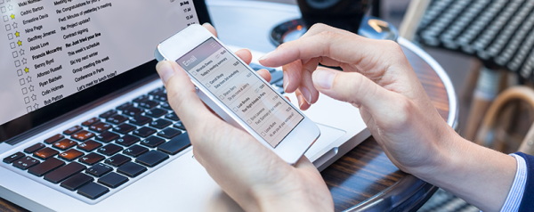 A hand holds a smartphone in front of a laptop.