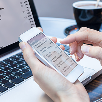 A hand holds a smartphone in front of a laptop.