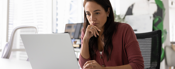 A woman works on a laptop at her desk while reviewing documents and reports.