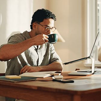This image shows a man drinking coffee sitting on his office desk looking on his laptop.