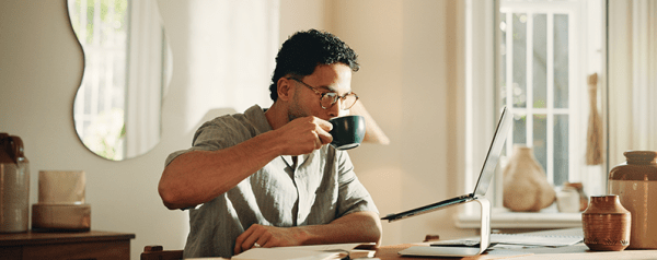 This image shows a man drinking coffee and working on his laptop.