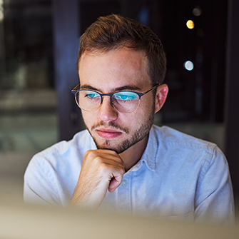 A man wearing glasses looks into a computer screen.