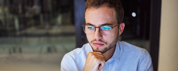 A man wearing glasses looks into a computer screen.
