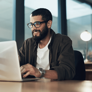 A man smiling in front of his laptop