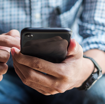 A seated person holds a smartphone in one hand and scrolls with the other.