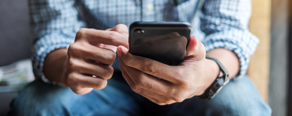 A seated person holds a smartphone in one hand and scrolls with the other.