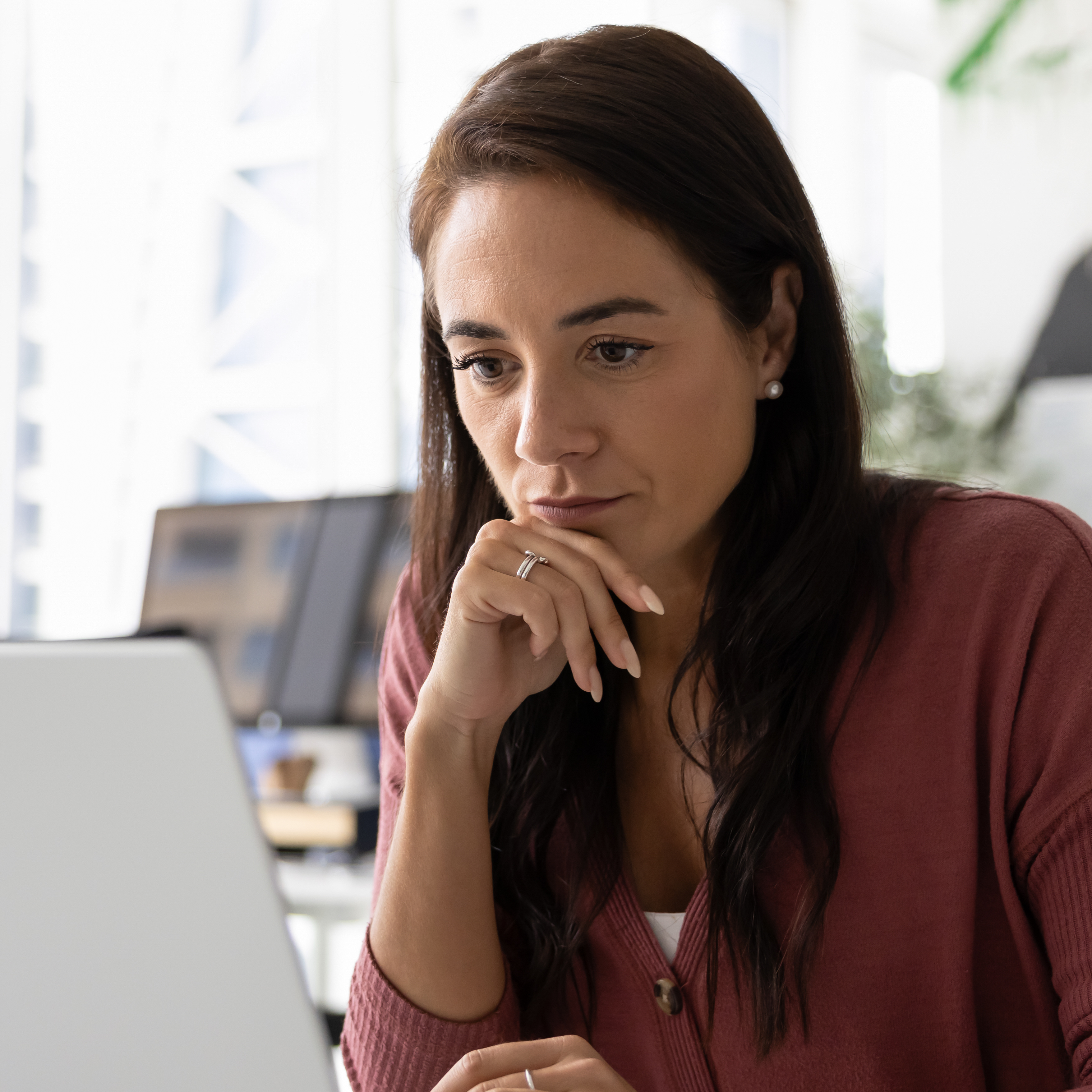 Image of a woman thinking while looking at a laptop.