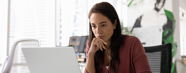Image of a woman thinking while looking at a laptop.