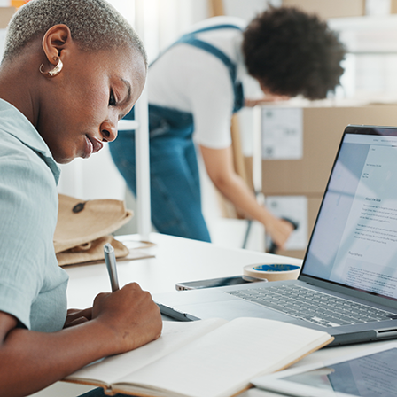 Two people at work, one is writing notes and the other is scanning a barcode on a package.