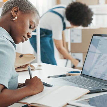 Two people at work, one is writing notes and the other is scanning a barcode on a package.