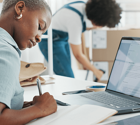 Two people at work, one is writing notes and the other is scanning a barcode on a package.