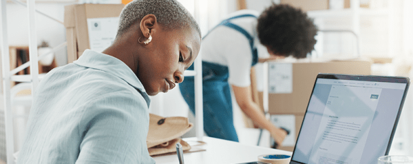 Two people working, one writing down notes and the other scanning a barcode on a package.