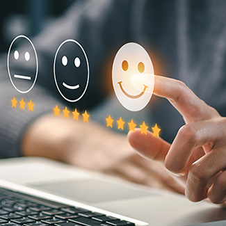 A person sits at a laptop as a rating system with stars and smiley faces hovers in the air.
