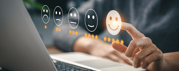 A person sits at a laptop as a rating system with stars and smiley faces hovers in the air.