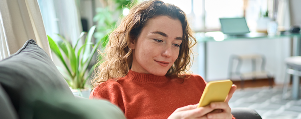 A woman in an orange sweater holds a smartphone and looks at the screen.