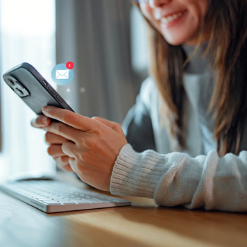 A woman holds a smartphone with a "1 new email" icon.