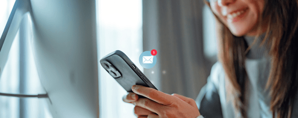 A woman holds a smartphone with a "1 new email" icon.