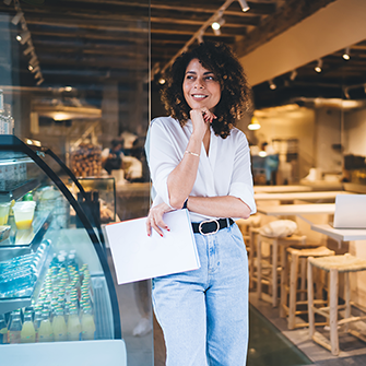 Woman holding a folder and smiling inside a bright cafe setting.