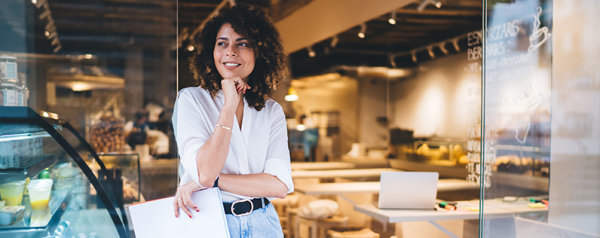 Woman holding a folder and smiling inside a bright cafe setting.