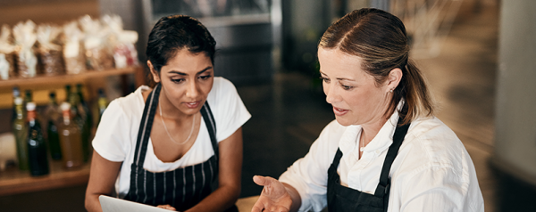 Two women in aprons look at a laptop screen.