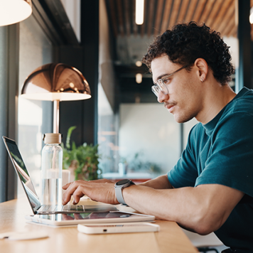 A man with glasses sits at a counter looking at a laptop screen.