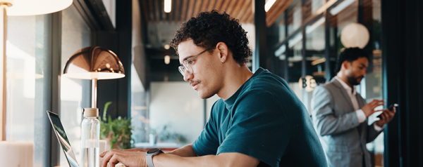 A man with glasses sits at a counter looking at a laptop screen.