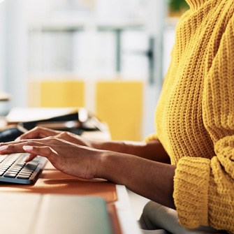 A woman in yellow typing on a keyboard