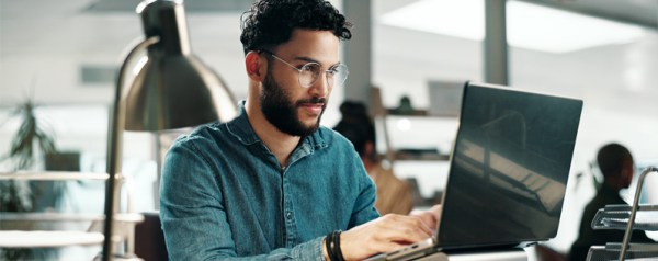 A man with a beard and glasses works at his computer.