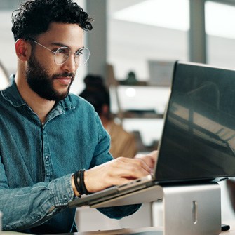 A man with a beard and glasses works at his computer.