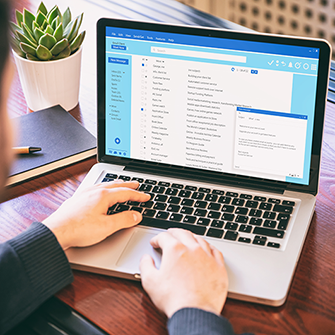 A person viewing an open email client inbox on a laptop screen at a desk.