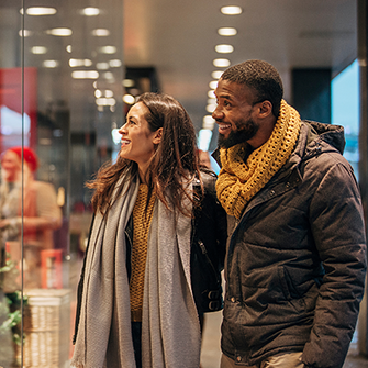 A woman and a man wearing coats and scarves look in a store window.