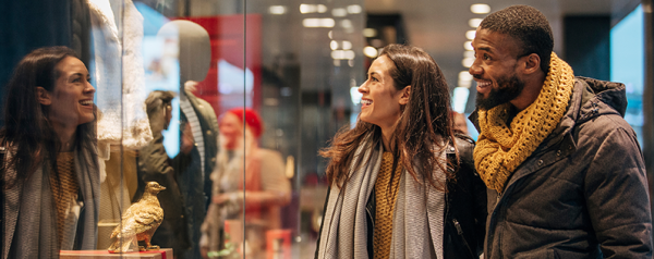 A woman and a man wearing coats and scarves look in a store window.