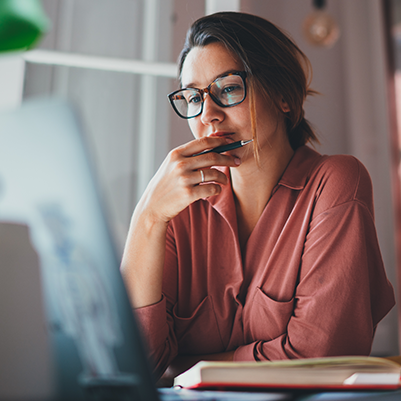 A woman in glasses sits in front of a desktop computer.