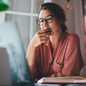 A woman in glasses sits in front of a desktop computer.