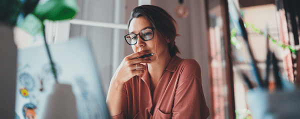 A woman in glasses sits in front of a desktop computer.
