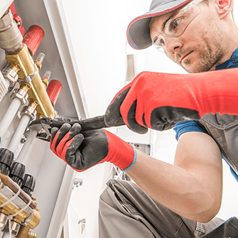 A tradesman wearing safety goggles uses a wrench on a pipe.
