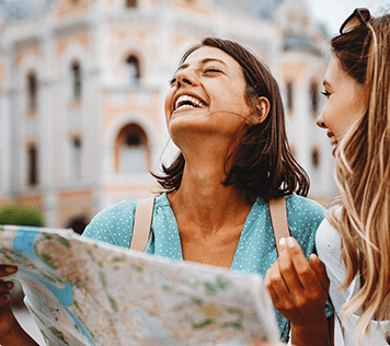 Two women travelers stand in a town square looking at a map.