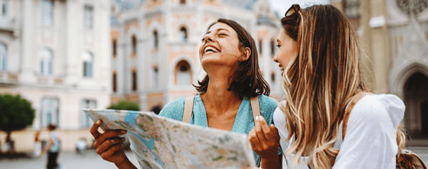 Two women travelers stand in a town square looking at a map.