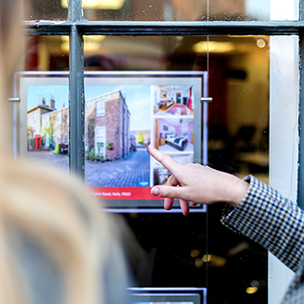 A hand points to a property listing in a window.