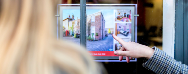 A hand points to a property listing in a window.