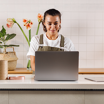 A florist works on her laptop surrounded by floral arrangements.
