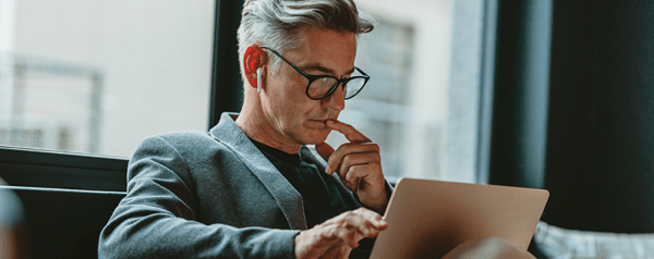 A man wearing earbuds sits in a chair looking down at his laptop.