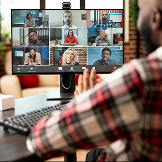 A man sits in front of a computer monitor displaying a video call with nine attendees.