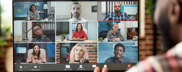 A man sits in front of a computer monitor displaying a video call with nine attendees.