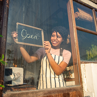 A woman inside a storefront hangs out an 'Open' sign.