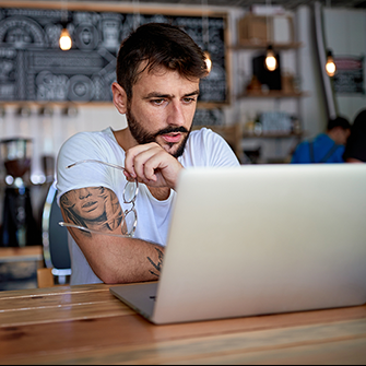 A man sits at the bar in a coffee shop in front of his laptop.