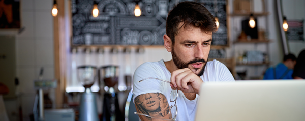 A man sits at the bar in a coffee shop in front of his laptop.