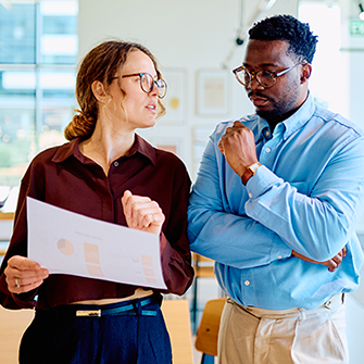 A man and a woman stand in an office looking down at a sheet of paper.