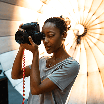A photographer holds a camera and puts their eye to the viewfinder.